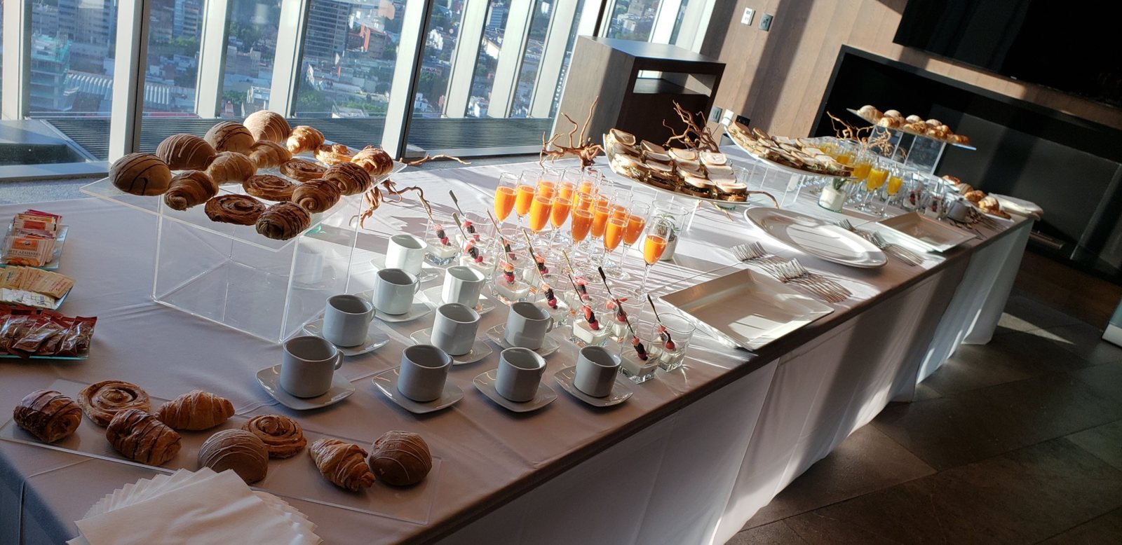 Coffee break junto a un ventanal con pan dulce, jugos, tazas y vasitos de yogur