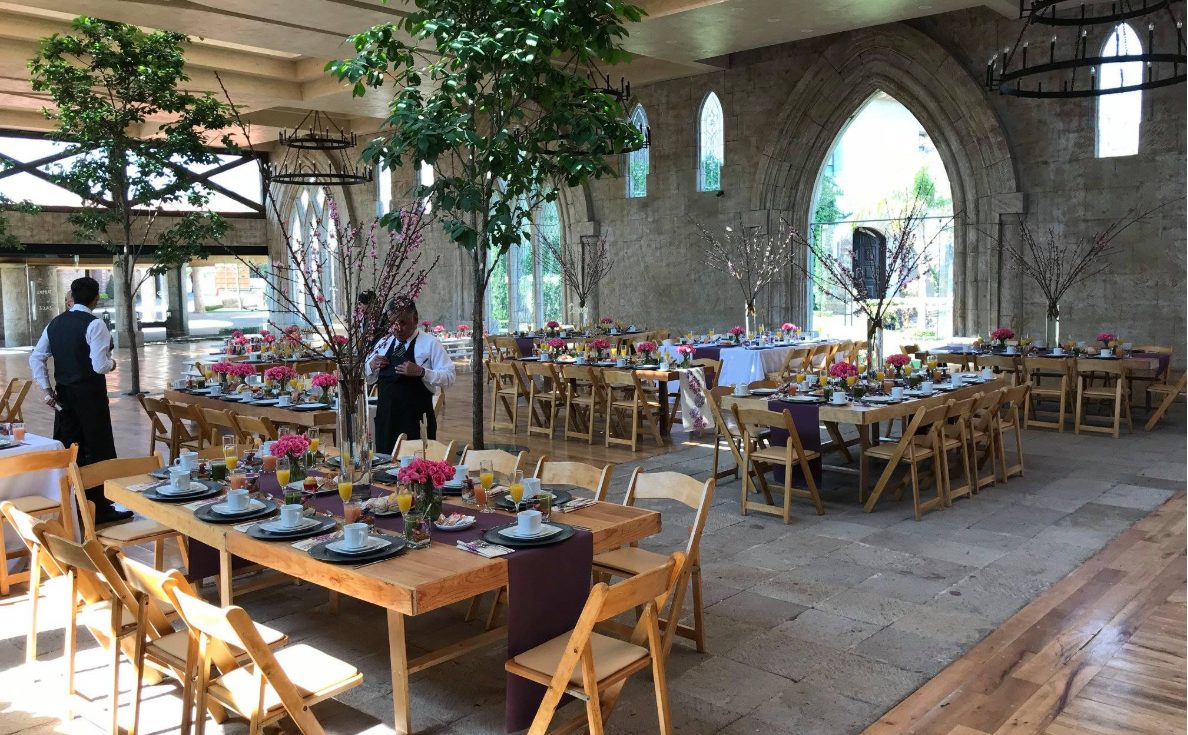 Montaje de desayuno en salón de arcos con mesas de madera y flores