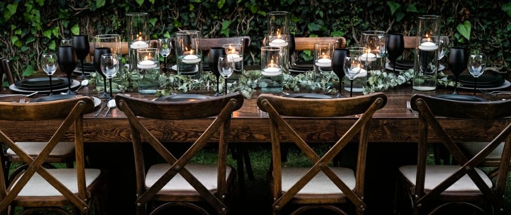Mesa con vajilla negra, velas flotantes y sillas de madera en jardín
