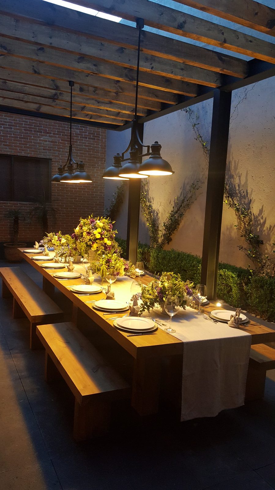 Mesa larga bajo pérgola con lámparas colgantes