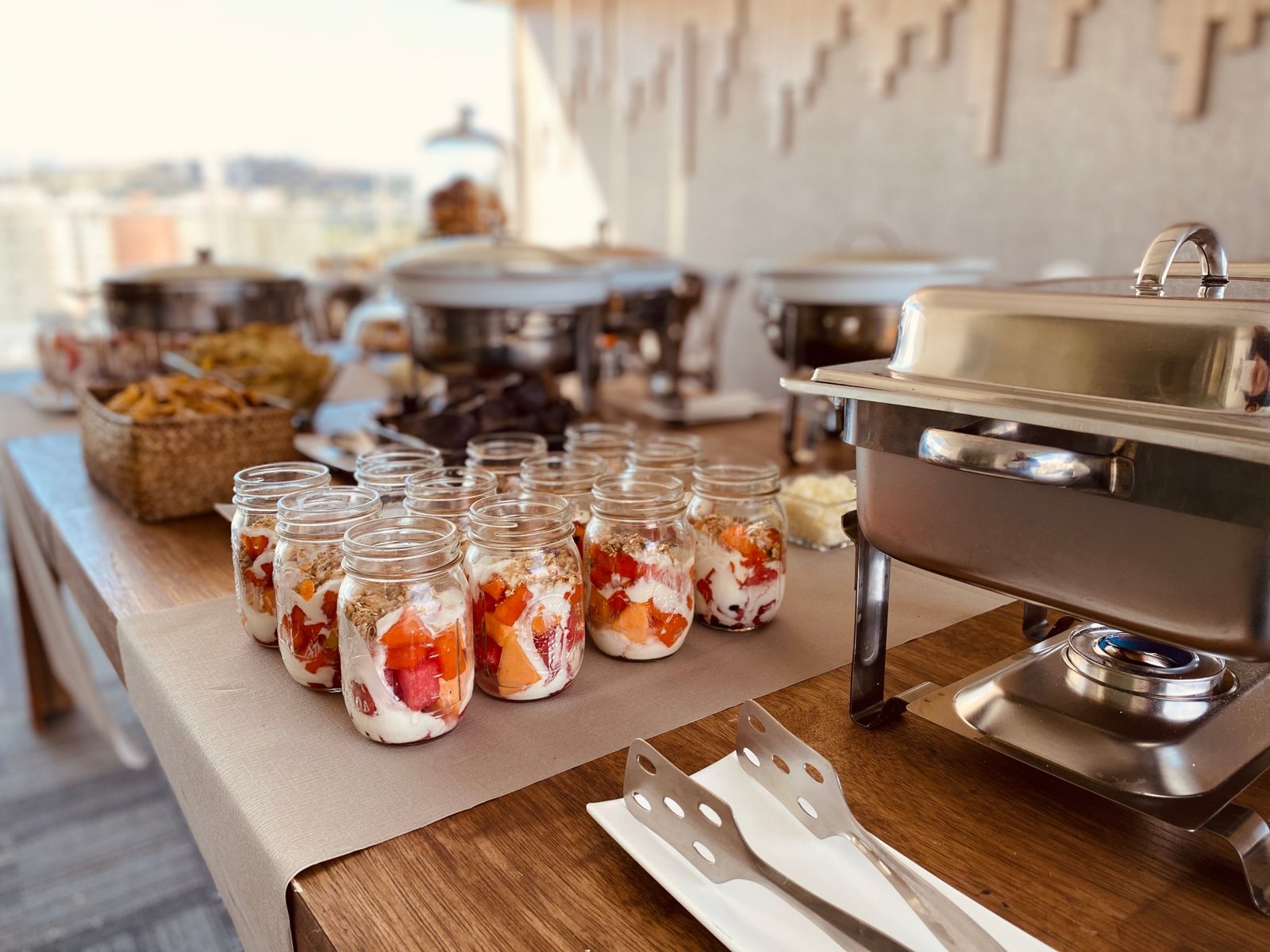 Barra de desayuno con vasitos de yogur y fruta junto a chafers en locación